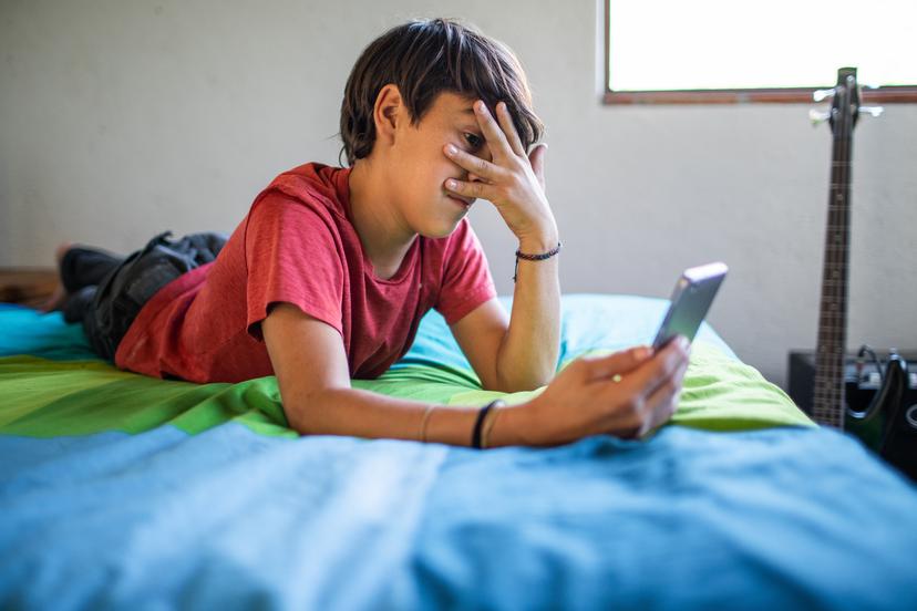 Boy covers eyes, afraid to look at something on smartphone screen